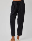 A person wears Bella Dahl’s high-waisted, black Lyocell-Leinen relaxed-fit jogger pants with elastic waistband and drawstring, styled with light open-toe slides. The plain background is light; the image is cropped at the waist.