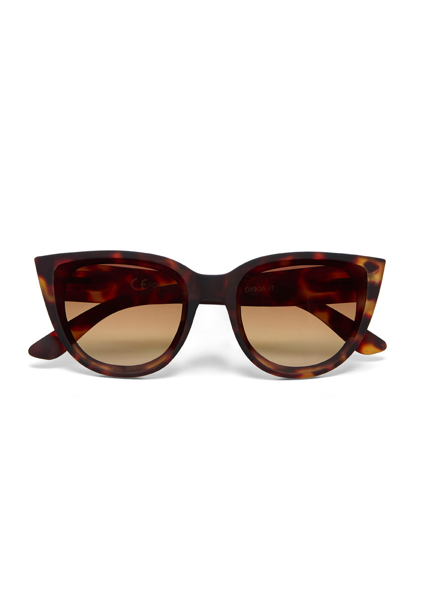 Front view of Okkia Cat-Eye-Sonnenbrille with a thick, brown and amber tortoiseshell frame. The UV-Schutz lenses show a subtle gradient from dark to light brown. Bold, retro-inspired style.