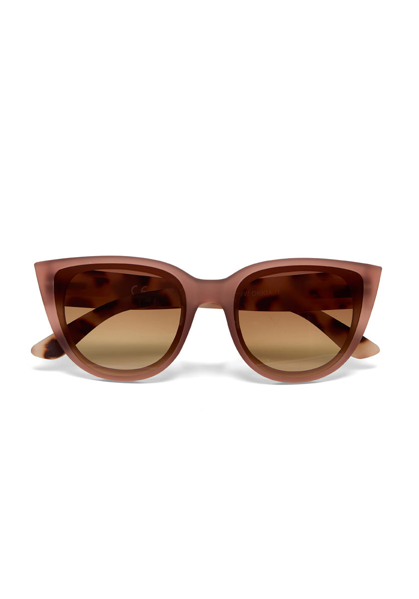 Front view of Okkia brown Cat-Eye sunglasses with wide, angular frames, dark brown gradient lenses, and a soft-touch finish. Slightly curved arms and full UV protection provide comfort and eye safety against a white background.