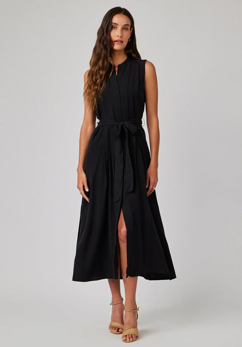 A woman with long wavy brown hair wears a sleeveless black Bella Dahl Lyocell midi dress with a tie belt and front slit. She stands facing forward in nude strappy sandals against a plain light gray background.