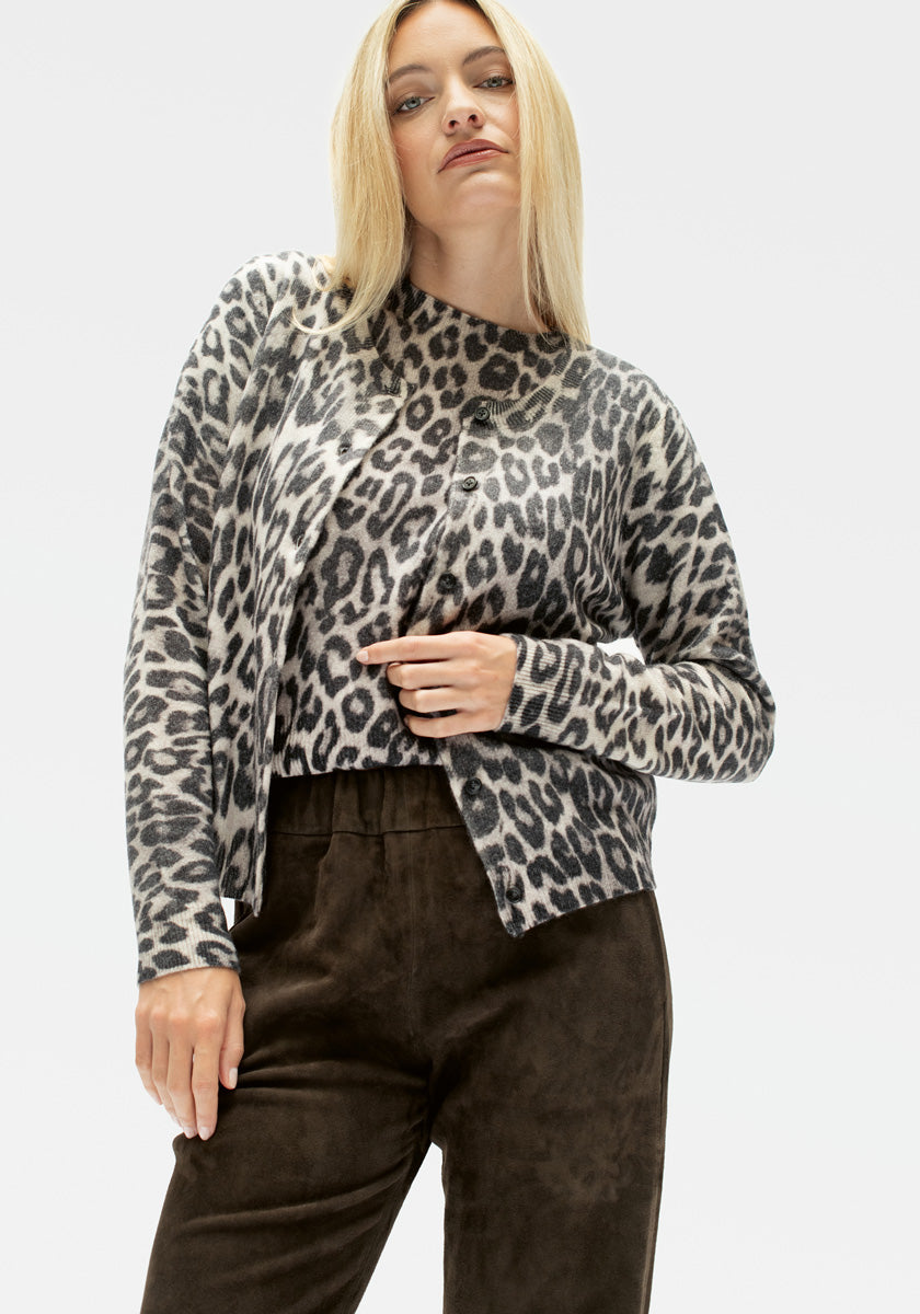 Ein Model mit glattem blondem Haar trägt eine grau-schwarze Leo-Print Kaschmir Strickjacke und ein dazu passendes Oberteil von Princess Goes Hollywood, gepaart mit einer hochtaillierten dunkelbraunen Wildlederhose, vor einem schlichten weißen Hintergrund.