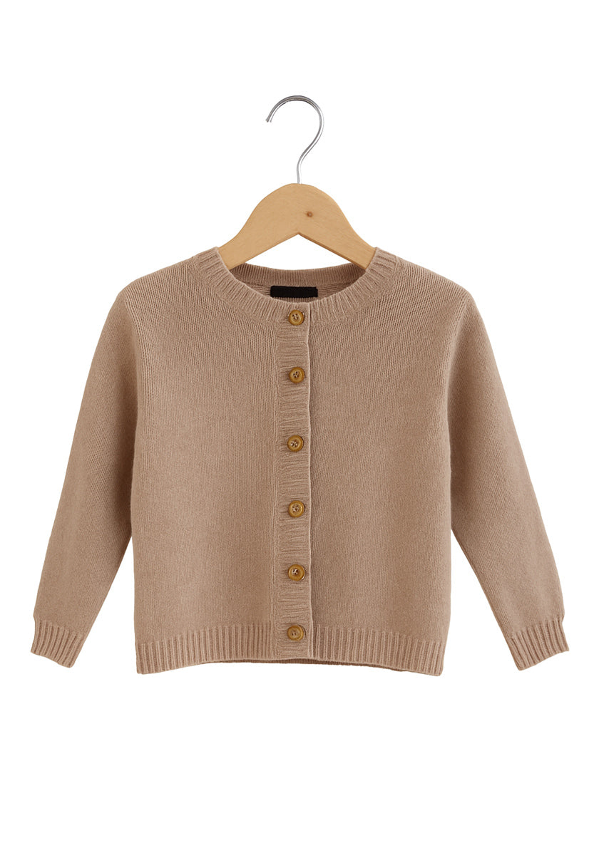 Eine beigefarbene, langärmelige Strickjacke von Princess Goes Hollywood hängt an einem Holzbügel. Sie hat einen Rundhalsausschnitt, fünf braune Knöpfe, gerippte Bündchen, Saum und Halsausschnitt. Dieser einfarbige Strick ist weich und kuschelig für Kinder.