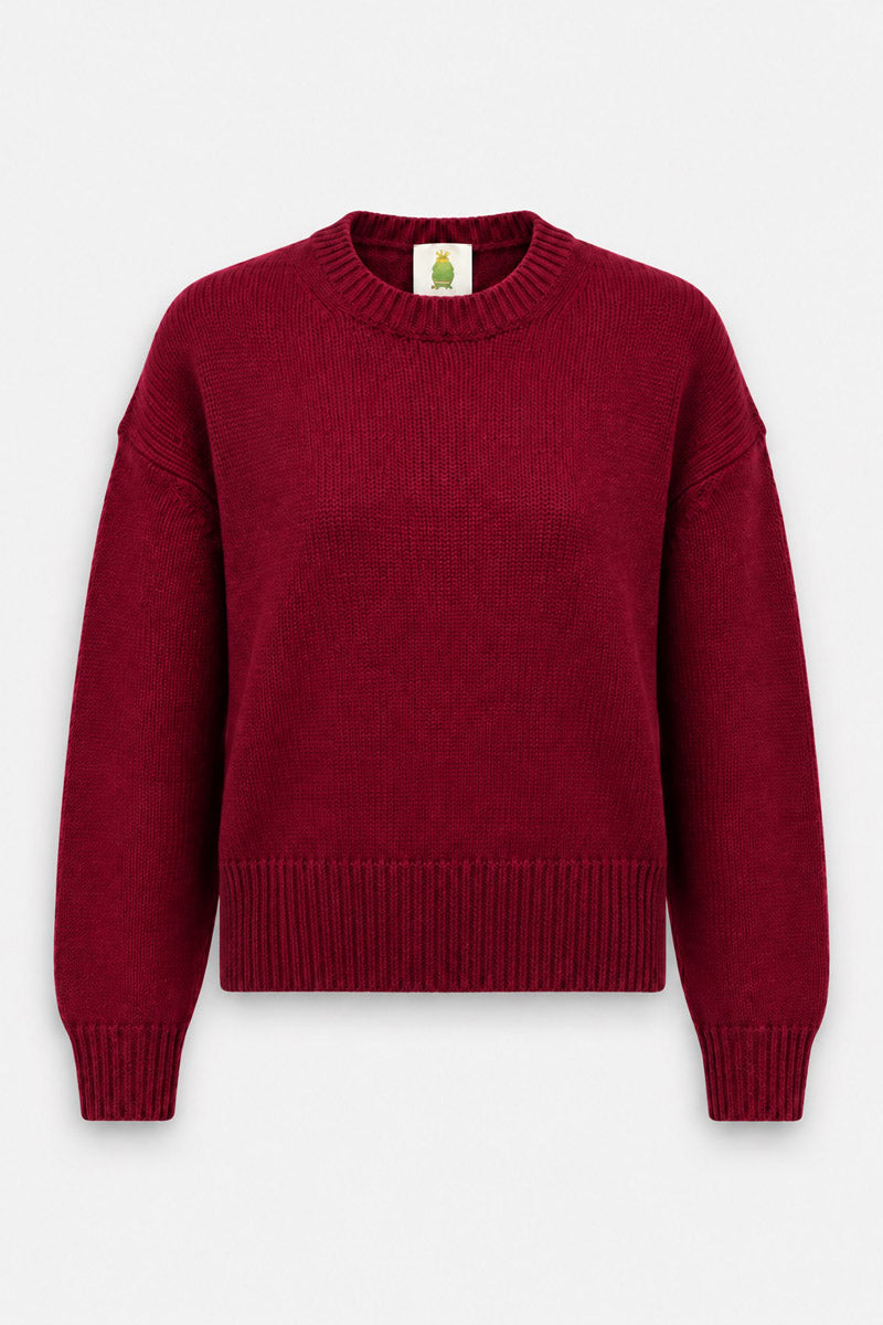 Ein tiefroter, langärmeliger Kaschmirpullover mit Rundhalsausschnitt, gerippten Ärmelbündchen und Saum. Das Strickteil ist mittig auf einem weißen Hintergrund abgebildet und verfügt über ein kleines Etikett am inneren Halsausschnitt mit einer illustrierten grünen Figur.