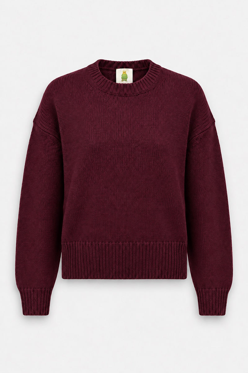 Ein langärmeliger, tief weinroter Kaschmir-Strickpullover mit Rundhalsausschnitt. Der Pullover hat gerippte Bündchen und einen breiten Saum, die sich von einem schlichten weißen Hintergrund abheben.