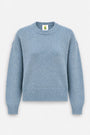 Ein staubblauer, langärmeliger Damenpullover mit geripptem Rundhalsausschnitt, geripptem Saum und gerippten Bündchen. Der locker sitzende Pullover hat überschnittene Schultern und ein kleines Etikett mit einer grünen Ananas-Grafik im Kragenbereich.