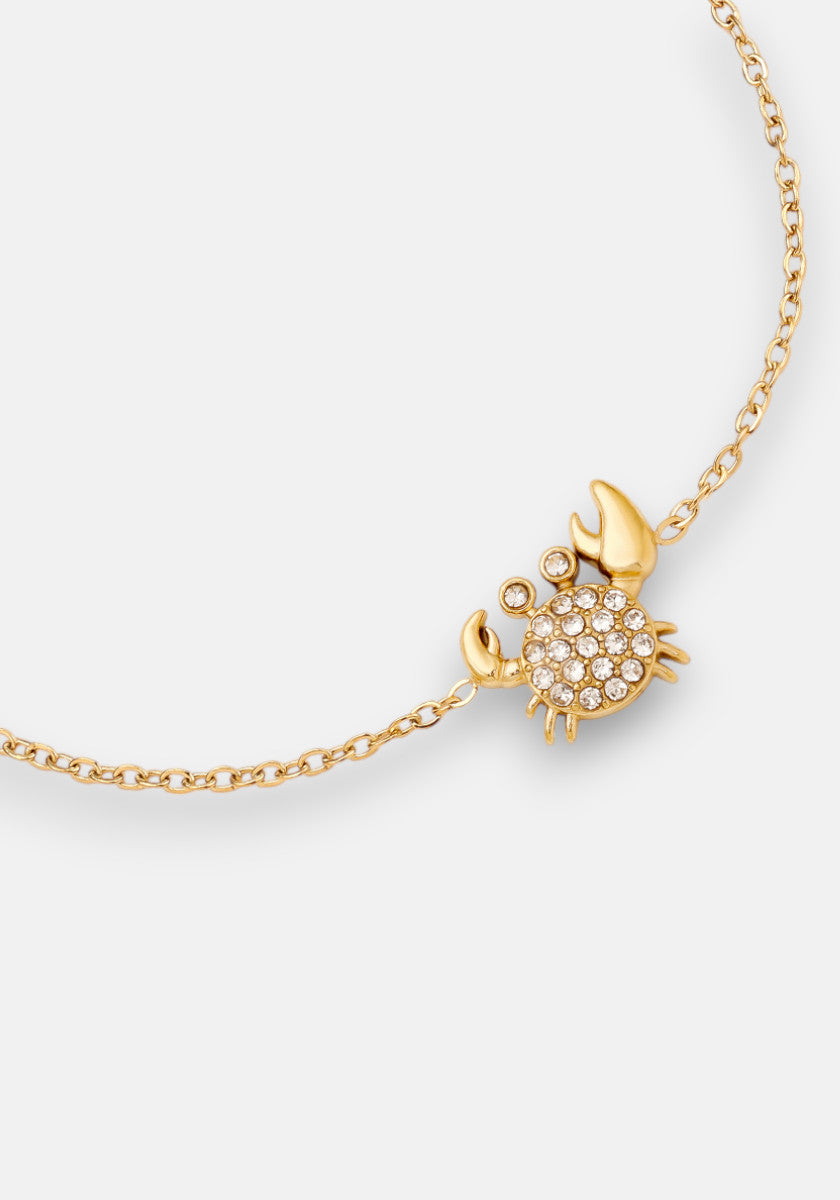 The Princess Goes Hollywood vergoldete Armkette features a small crab pendant with sparkling white gemstones and gold-tone claws and legs, creating a playful yet elegant accessory displayed on a plain white background.