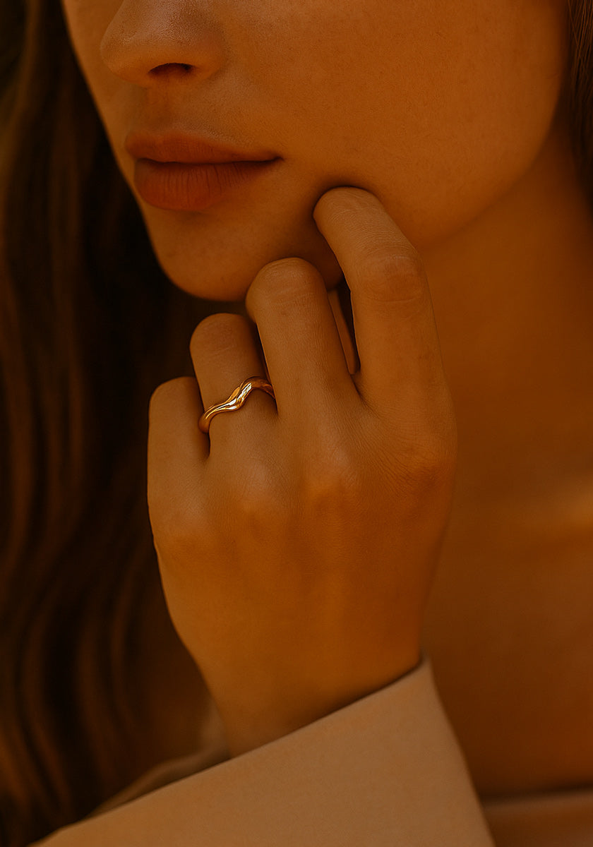A close-up of a person’s hand wearing a Princess Goes Hollywood offener Ring mit Gelbgold Vergoldung, gently touching their face. Soft light adds warmth and highlights the golden tones, with only the lower half of their face visible.
