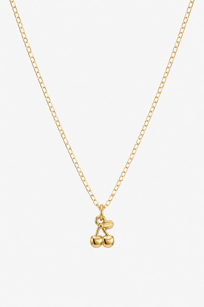 Eine schlichte Goldkette von Princess Goes Hollywood ist mit einem glänzenden „Kirsche“-Anhänger mit zwei Kirschen und einem Blatt verziert. So entsteht ein elegantes Schmuckstück aus Edelstahl, das vor einem schlichten weißen Hintergrund zu einem trendigen Accessoire wird.