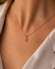 Eine Nahaufnahme zeigt eine Person in einer cremefarbenen Bluse, die den zarten goldenen „Kirsche“-Charm-Anhänger aus Edelstahl von Princess Goes Hollywood trägt; ihre glatte Haut bringt das trendige Accessoire am Ausschnitt besonders gut zur Geltung.