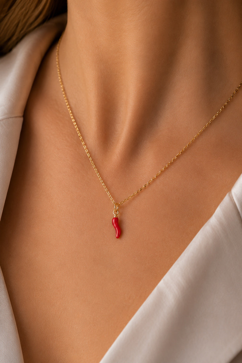 Nahaufnahme des Halses einer Frau, die eine goldene Kette von „Princess Goes Hollywood“ mit einem „Chili“-Anhänger als trendiges Accessoire trägt. Sie trägt ein weißes Hemd mit offenem Kragen, und ihr warmer Hautton unterstreicht den eleganten, minimalistischen Stil.