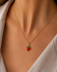 Eine Frau ist von den Schultern abwärts zu sehen; sie trägt einen hellbeigen Blazer und ein weißes Oberteil. Als Accessoire trägt sie eine goldene Kette der Marke „Princess Goes Hollywood“ mit einem kleinen Erdbeer-Anhänger, der mit grünen Blättern verziert ist.
