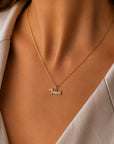 Nahaufnahme des Halses einer Frau, geschmückt mit der goldenen „Dackel Charm“-Halskette von Princess Goes Hollywood, die einen dackelförmigen Edelstahl-Anhänger aufweist. Sie trägt einen hellen Blazer; warmes Licht hebt dieses ideale Geschenk für Hundefans hervor.