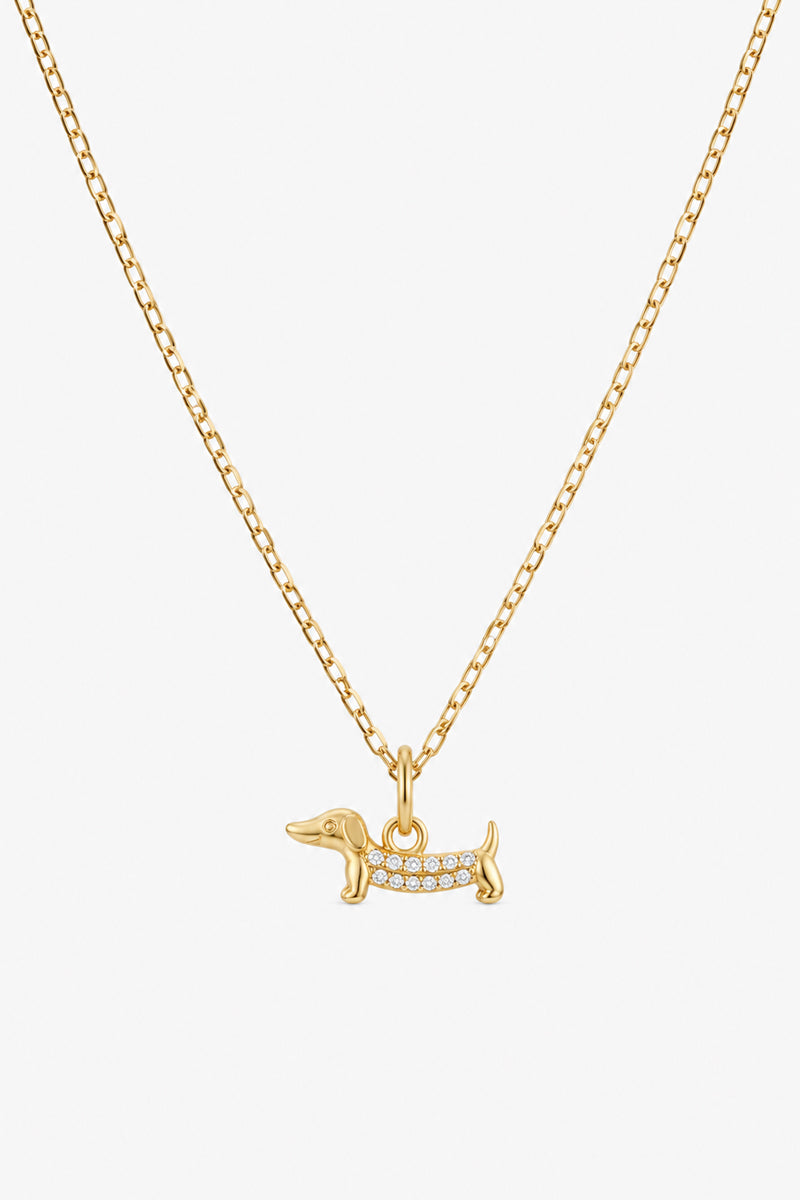 Die Goldkette „A Princess Goes Hollywood“ ist mit einem kleinen Dackel-Anhänger verziert, dessen Körper sowie Kopf, Schwanz und Beine aus poliertem Gold bestehen und mit funkelnden klaren Steinen besetzt sind – perfekt für Hundeliebhaber. Abgebildet auf einem schlichten weißen Hintergrund.