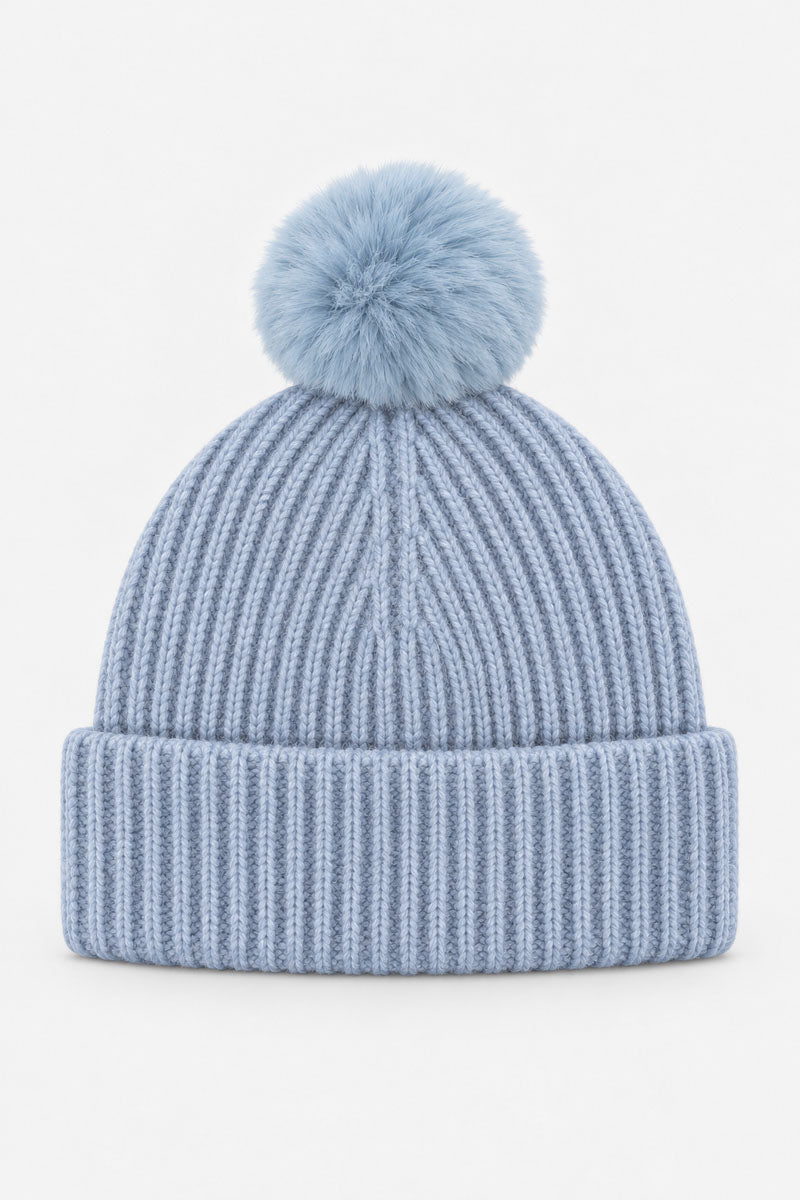 Eine hellblaue Rippstrick-Mütze mit einem passenden Bommel aus Kunstfell oben drauf. Die Wintermütze hat einen breiten, umgeschlagenen Rand und ist mittig auf einem schlichten weißen Hintergrund abgebildet.