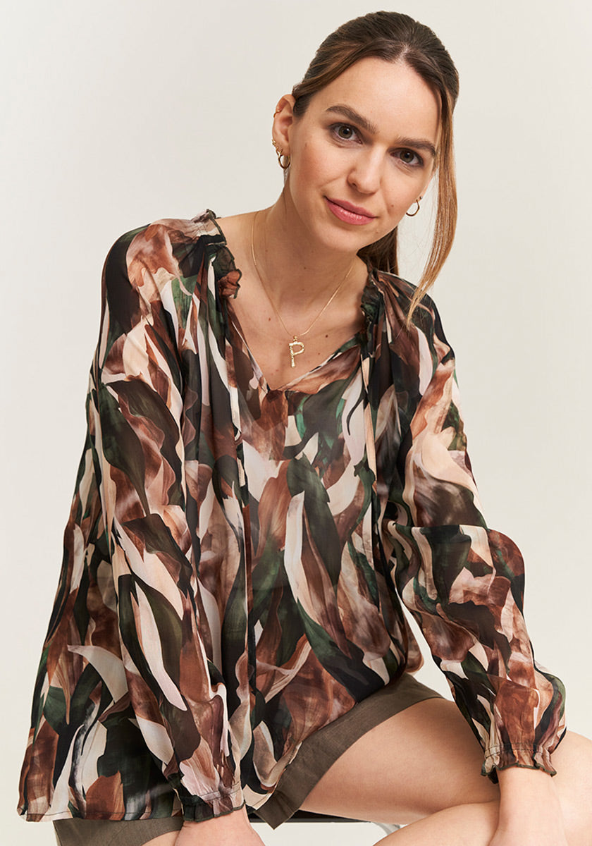 Lady wearing a blouse made of flowing fabric with leaf pattern with long sleeves in summer