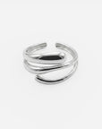 Ein glänzender silberner Edelstahlring von Princess Goes Hollywood mit offenem Banddesign und zwei eleganten, sich überlappenden Kurven, die sich an der Vorderseite ineinander verschlingen. Dieser verstellbare Ring besticht durch seinen minimalistischen Look und wird vor einem schlichten weißen Hintergrund fotografiert – ein perfektes Schmuckstück für Liebhaber von modernem Schmuck.