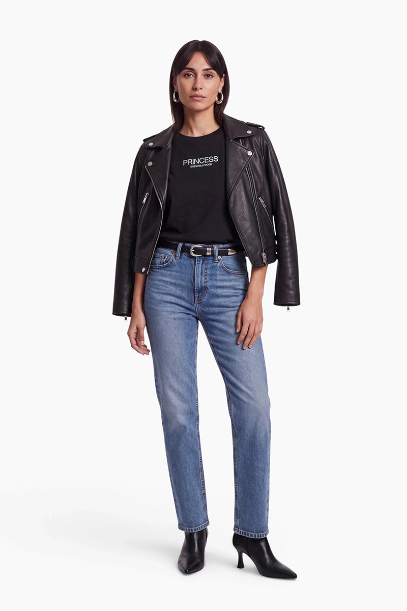 Eine Frau trägt eine schwarze Lederjacke über einem Baumwoll-T-Shirt der Marke Princess Goes Hollywood. Dazu kombiniert sie eine hellblaue Jeans, einen schwarzen Gürtel mit einer Schnalle in Metallic-Optik und schwarze Stiefel mit Absatz vor einem weißen Hintergrund.