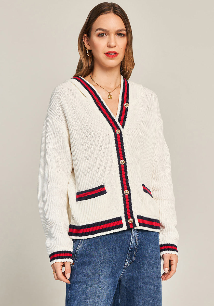 A woman with straight brown hair wears a white Princess Goes Hollywood cardigan featuring red and navy trim on the collar, cuffs, pockets, and button band. She pairs it with blue jeans and faces forward against a neutral background.