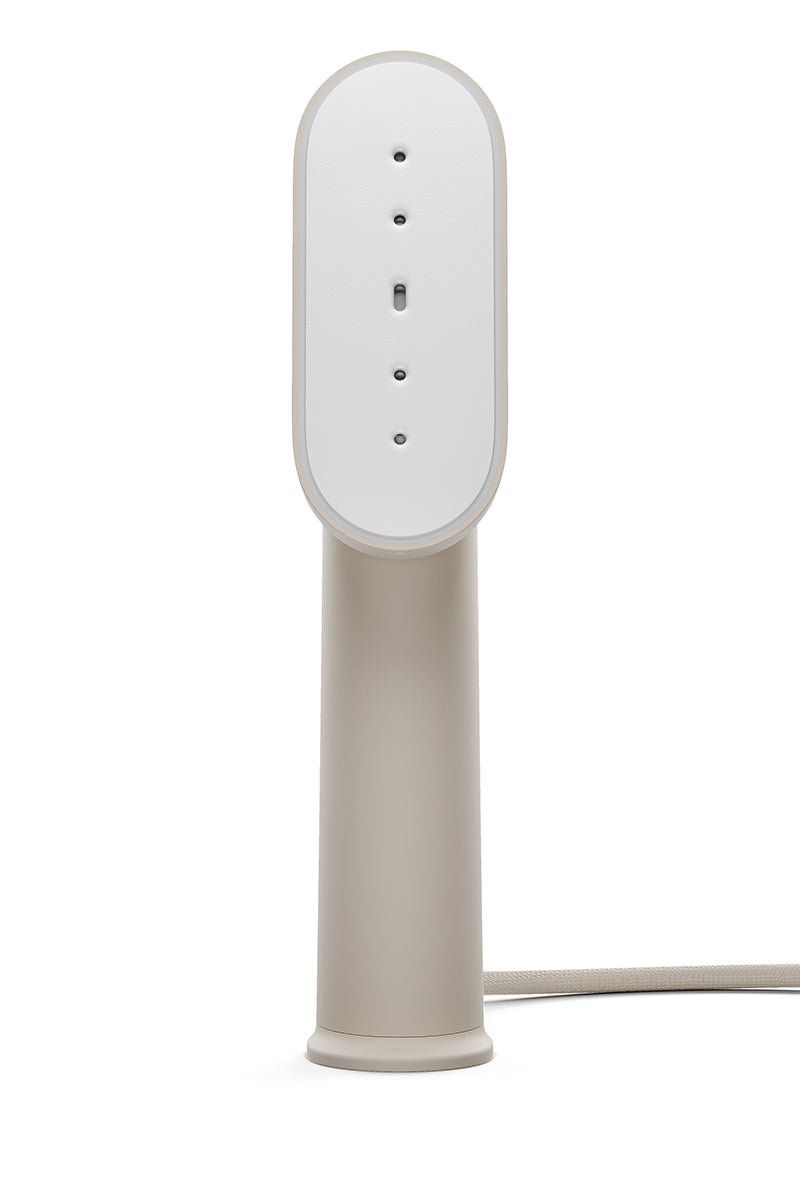 Der Steamery tragbarer Dampfglätter besticht durch sein minimalistisches Design mit einem schlanken, beigen, zylindrischen Griff, einem ovalen, weißen Kopf mit fünf vertikalen Dampflöchern und einem stoffummantelten Netzkabel - ideal für die Pflege von Kleidungsstücken unterwegs.