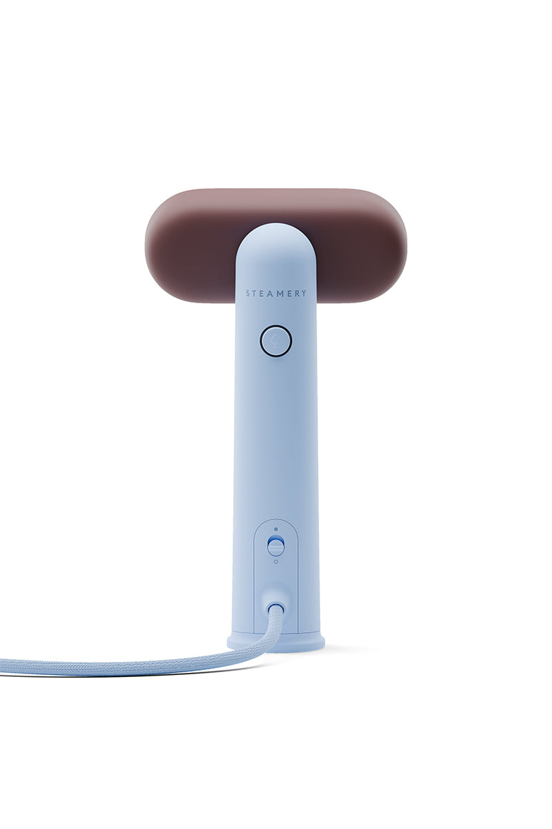 Der tragbare Kleidungsdampfer von Steamery hat einen hellblauen Griff, einen großen runden dunkelbraunen Dampfkopf und ein vertikales Steamery-Branding. Darunter hängt eine weiße Stoffkordel. Das Produkt ist vor einem weißen Hintergrund abgebildet.