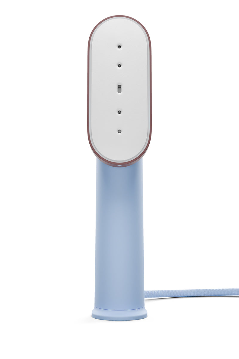 Die Steamery tragbarer Dampfglätter steht aufrecht mit einem glatten, hellblauen zylindrischen Griff, einem weißen ovalen Dampfkopf mit kleinen Löchern und einer blauen Kordel, die vom Sockel ausgeht. Der Hintergrund ist einfarbig weiß.