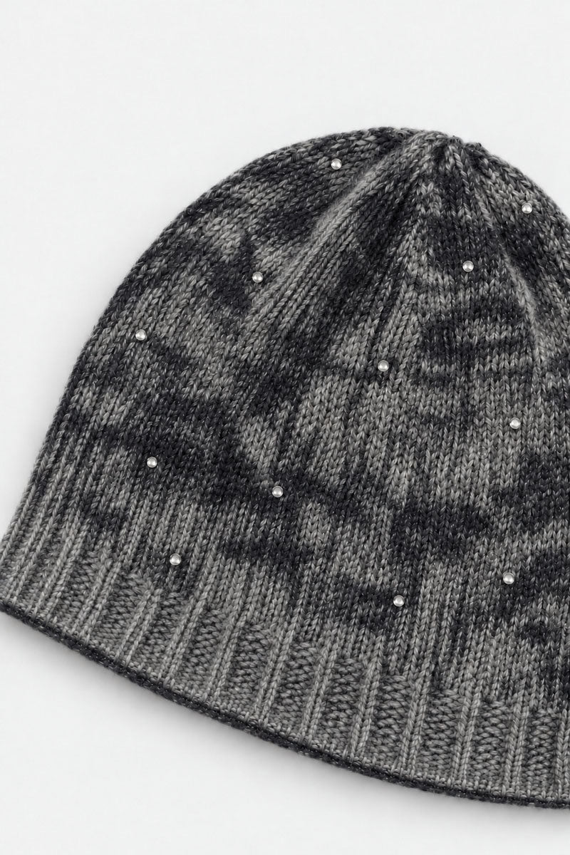 Eine grau-schwarz melierte Strickmütze, die mit vereinzelten silbernen Nieten verziert ist. Die Mütze verfügt über einen gerippten Rand und eine weiche, melierte Struktur mit zarten Strassverzierungen auf schlichtem weißem Hintergrund.