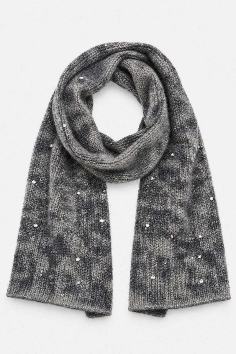 Ein grauer, melierter Strickschal aus einer Merino-Kaschmir-Mischung ist oben zu einer Schlaufe gebunden und hängt an zwei Enden herab. Das weiche, flauschige Material wird durch vereinzelte Strasssteine vor einem schlichten weißen Hintergrund akzentuiert.