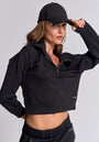 A woman in a black zippered crop top and matching pants poses with one hand on her hip, adjusting a schwarze Kappe mit PRINCESS-Schriftzug by Princess Goes Hollywood against a plain light gray background.