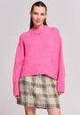 A woman stands against a light grey background, wearing a bright pink Princess Goes Hollywood Kaschmir Pullover mit Stehkragen and a high-waisted green-and-pink plaid skirt. She has straight brown hair pulled back, gold earrings, and smiles subtly with hands at her sides.