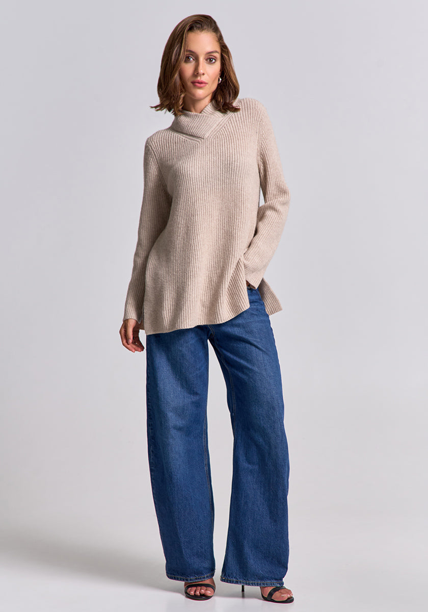 A woman with chin-length brown hair poses confidently in a Princess Goes Hollywood wool-cashmere blend cowl-neck sweater with long sleeves, wide-leg blue jeans, and black open-toe heels against a light-gray background.