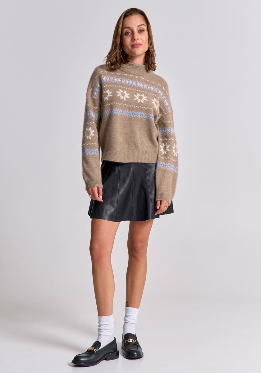 A woman with shoulder-length brown hair and a neutral expression wears a Princess Goes Hollywood Jacquard pullover with white and blue snowflakes and Stehkragen, styled with a black leather mini skirt, white socks, and black loafers against a plain gray background.
