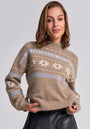 A woman with light brown, shoulder-length hair smiles softly, wearing a beige Princess Goes Hollywood Jacquarpullover with white and light blue snowflake patterns and a Stehkragen, paired with a black leather skirt against a plain light gray background.