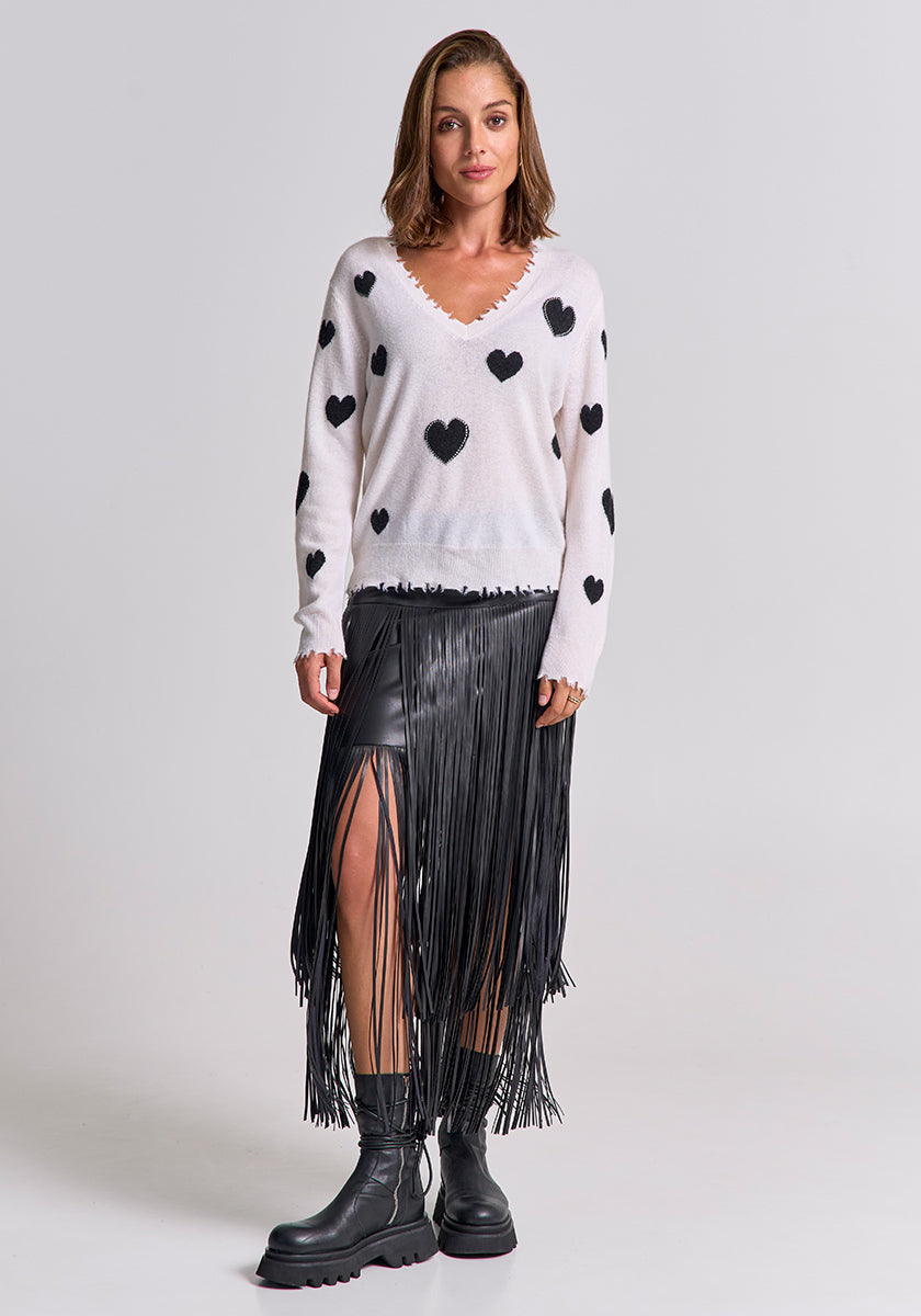 A woman with shoulder-length brown hair poses in a Princess Goes Hollywood Feinstrickpullover with Herz-Muster, a black faux leather fringe skirt, and chunky black boots against a plain background, exuding relaxed style and a neutral vibe.