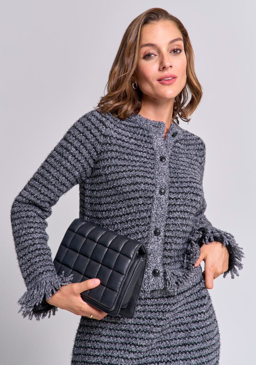 A woman with shoulder-length brown hair wears a gray bouclé button-up Strickjacke and matching skirt from Princess Goes Hollywood, holding a black quilted handbag under her arm, standing confidently against a plain light gray background.