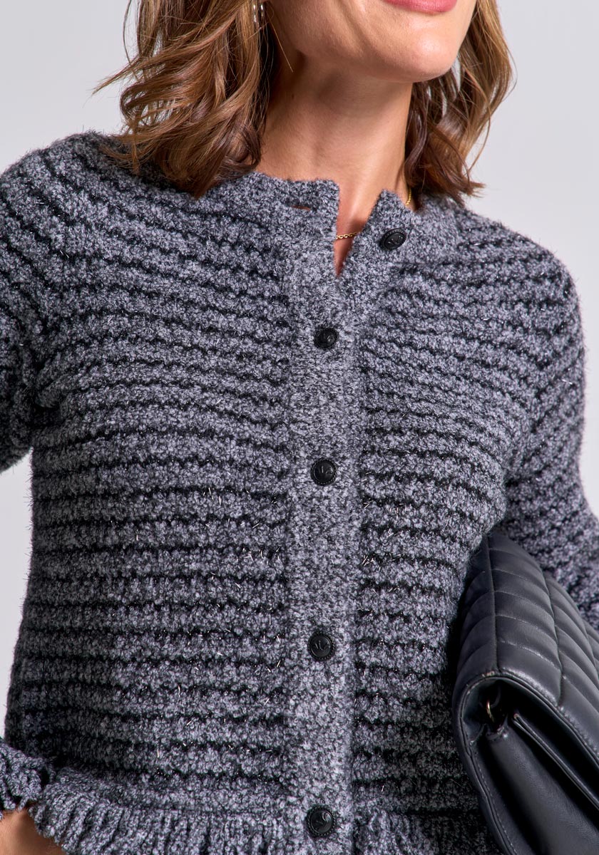 A woman with shoulder-length, wavy brown hair wears a textured gray Princess Goes Hollywood Bouclé-Style Strickjacke and holds a black quilted handbag under her arm. Only her torso and smiling face are shown against a plain background.