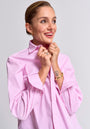A smiling woman with short, slicked-back hair holds the collar of her pink and white gestreift Regular Fit Baumwollhemd from Princess Goes Hollywood. She wears gold jewelry and has a heart tattoo on her left wrist against a light gray background.