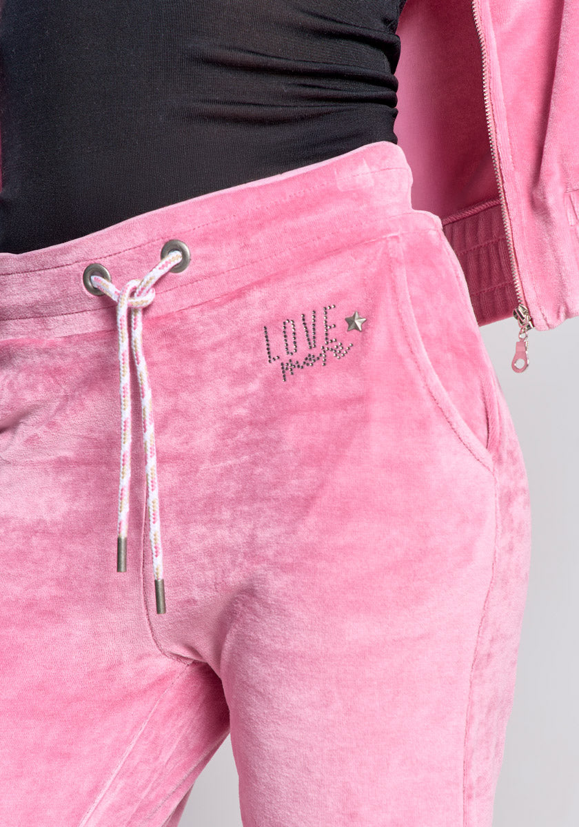 A person wears Princess Goes Hollywood soft pink Nicki-Stoff sweatpants with a drawstring waist, side pocket, LOVE and a star with strass detail on the left hip, paired with a black top and matching pink jacket.