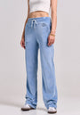 Someone stands against a plain background wearing light blue Princess Goes Hollywood Sweatshose aus Nicki-Stoff with a drawstring waist and “LOVE” graphic on the hip, paired with a white crop top, white sneakers, and a gold bracelet. Their face is not visible.