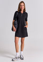 A woman with shoulder-length brown hair smiles against a plain background, wearing a Princess Goes Hollywood short-sleeved Mini Sweatkleid with front zipper, white socks, athletic sneakers, and carrying a black shoulder bag. One hand is in her pocket.