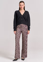 A woman faces forward wearing a black buttoned cardigan, Princess Goes Hollywood Glam-Leo-Print wide-leg pants with an elastic waist, and black pointed-toe heels. She accessorizes with layered gold necklaces and a bracelet.