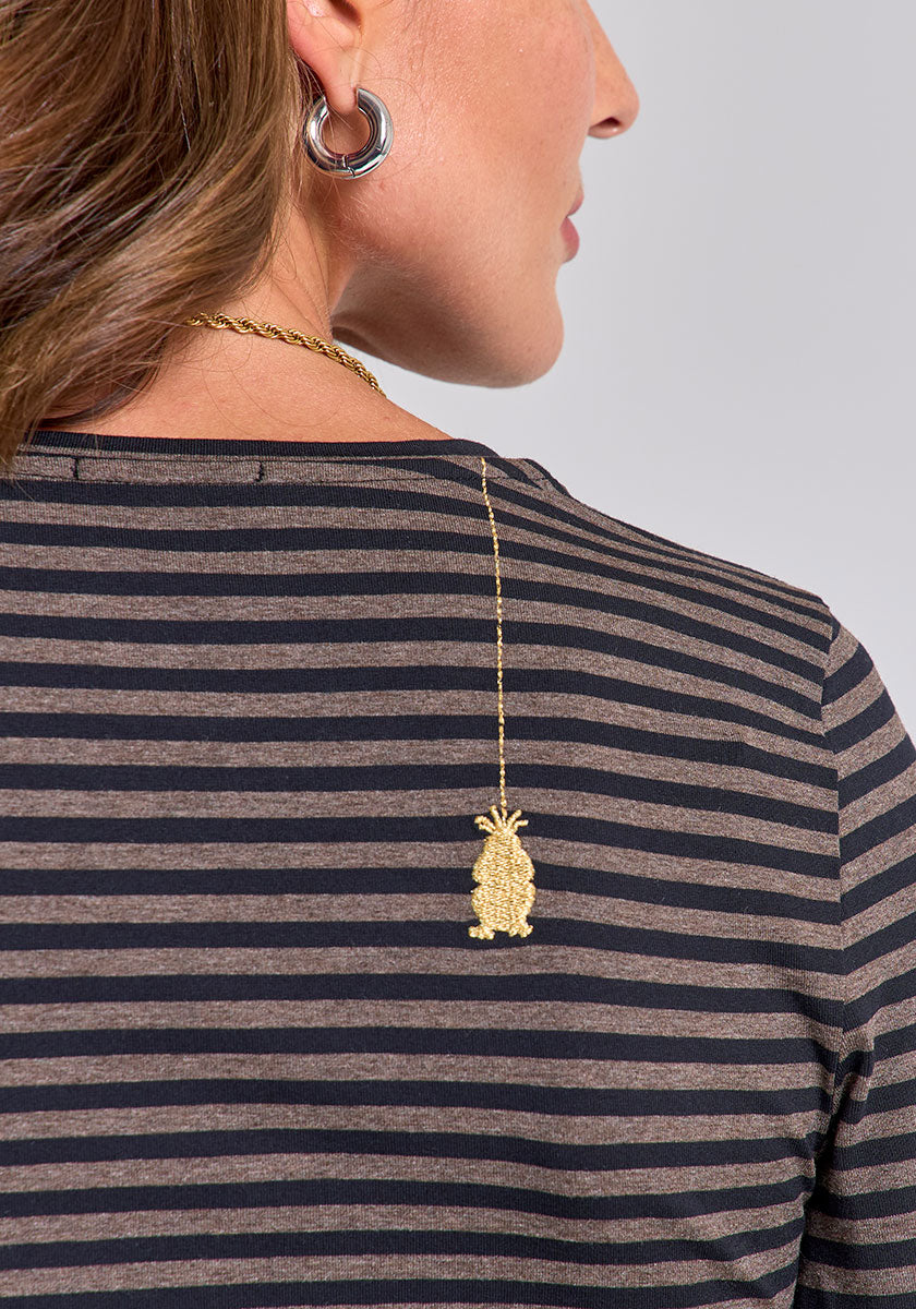 A woman with brown hair wears a black and brown gestreiftes Langarmshirt by Princess Goes Hollywood. She pairs it with a gold pineapple pendant necklace, twisted gold chain, large silver hoop earring, and stands against a light gray background.