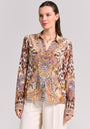 A woman with fair skin and brown hair tied back models a Princess Goes Hollywood Seidenbluse with Snake-Leo-Print and paisley in brown, beige, and gold, paired with cream pants and gold jewelry against a light background.