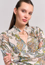 A woman with light skin and straight brown hair pulled back poses with arms crossed, wearing a Princess Goes Hollywood paisley-print blouse with a smocked stand collar, gold hoop earrings, and layered necklaces against a light background.