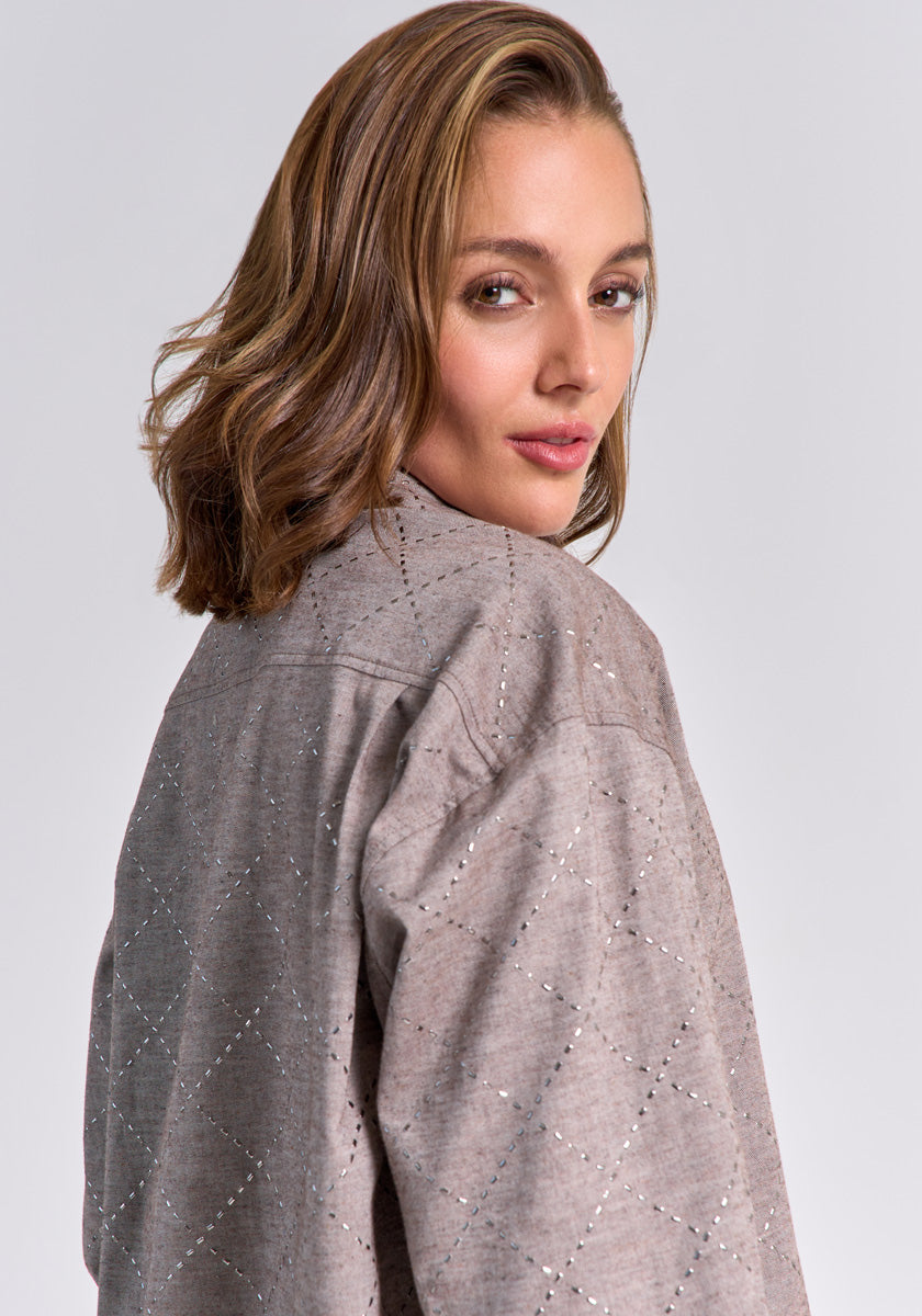 A woman with wavy, shoulder-length light brown hair looks back at the camera wearing a light gray, quilted Princess Goes Hollywood jacket with a subtle diamond pattern and small perforations. The background is plain light gray.