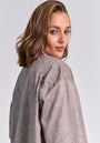 A woman with wavy, shoulder-length light brown hair looks back at the camera wearing a light gray, quilted Princess Goes Hollywood jacket with a subtle diamond pattern and small perforations. The background is plain light gray.