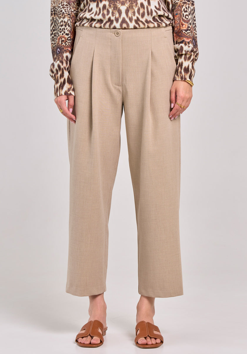 A person stands facing forward, wearing beige 7/8-length wide-leg pants by Princess Goes Hollywood, a long-sleeved brown animal-print top, brown flat sandals, and gold rings. The chest-cropped photo highlights the pants and shoes against a plain backdrop.