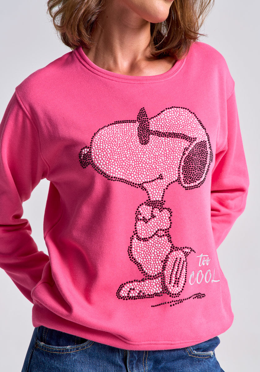 A woman models a Princess Goes Hollywood Snoopy sweatshirt with rhinestone embellishments and "too cool" in white below the cartoon dog. She pairs it with blue jeans, standing with her hands behind her back.