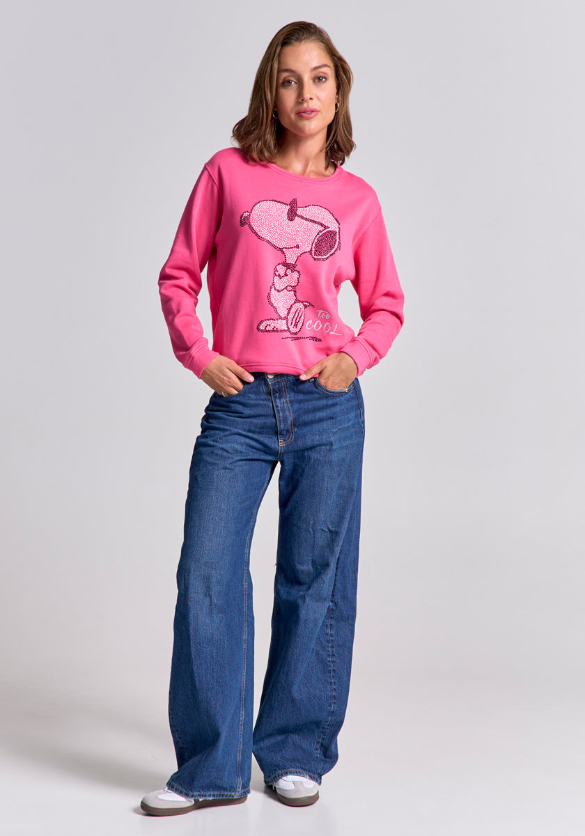 A woman with shoulder-length brown hair stands confidently with hands in her pockets, wearing a bright pink Princess Goes Hollywood Damen Snoopy Sweatshirt featuring an &quot;I&#39;m Cool&quot; graphic, blue wide-leg jeans, and white sneakers.