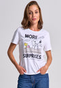 A woman with shoulder-length light brown hair wears a Princess Goes Hollywood Peanuts-Print Baumwolle T-Shirt featuring Snoopy and Woodstock on a doghouse with gifts and the phrase “MORE SURPRISES.” She pairs it with blue jeans against a plain background.