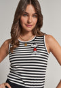 A young woman with wavy brown hair wears a striped, ribbed, sleeveless top with a small Snoopy print and Joe Cool lettering from Frogbox by Princess. Layered gold chains complete her confident look against a neutral background.
